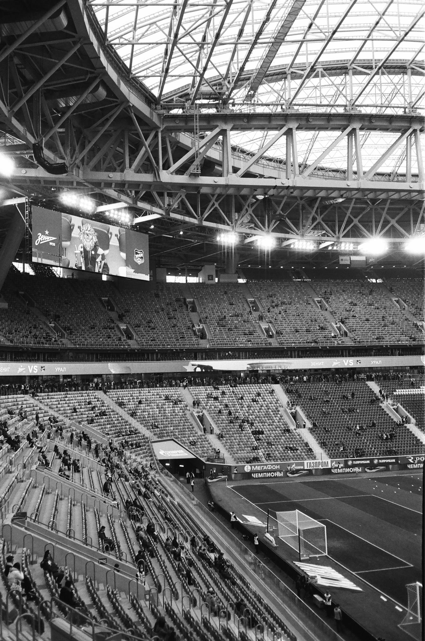 Black and white photo of a modern domed stadium with empty seats and a large screen.